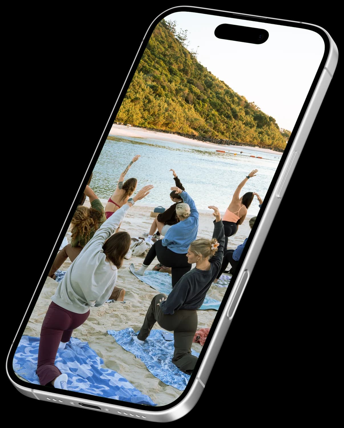 A Mikki’s Mobility class in warrior pose on the sand, shown on an angled iPhone.