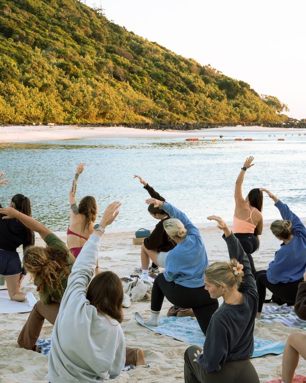 A Mikki’s Mobility class in warrior pose on the sand, the headland and sea behind them.