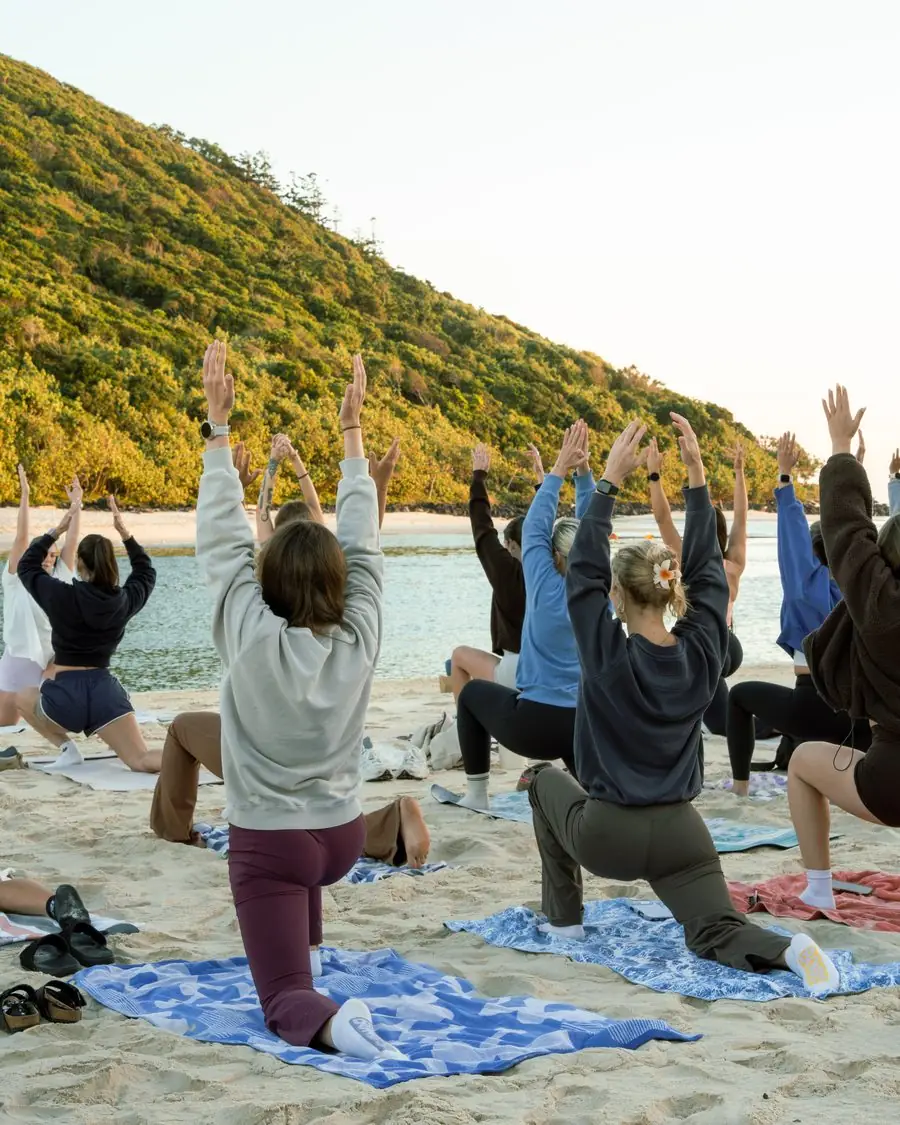 A Mikki's Mobility class on the sand with their arms raised to the sky, the headland behind them.